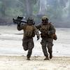 Two U.S. Marines in uniform run in the sand, with one carrying a missile launcher.