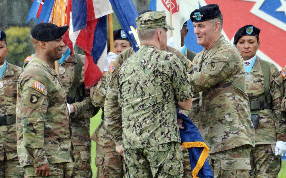 Army officers in camoflauge uniforms conduct a change-of-command ceremony in front of a flag corps.