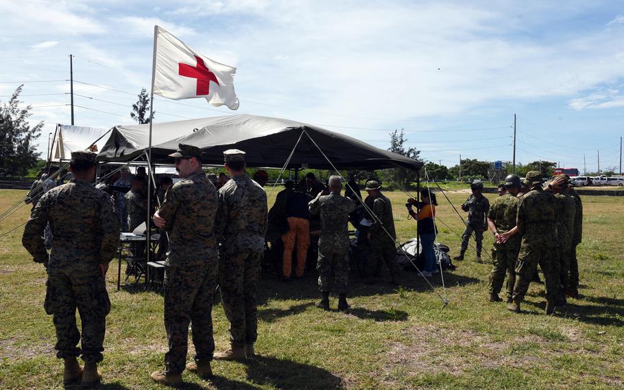 Troops stands outside of a tent with a white medical flag.