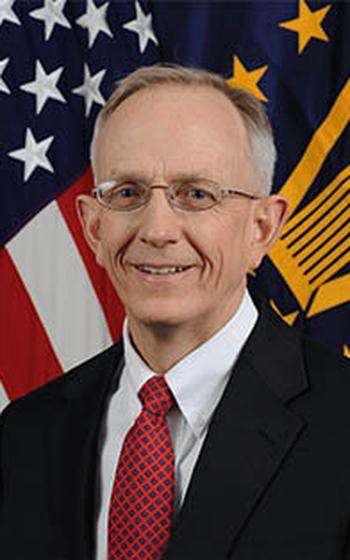 Photo of Smith in a suit standing in front of flags.