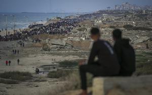 Two boys watch a crowd of Palestinians returning to northern Gaza, amid destroyed buildings, following Israel's decision to allow thousands of them to return for the first time since the early weeks of the 15-month war with Hamas, Monday, Jan. 27, 2025. (AP Photo/Abdel Kareem Hana)