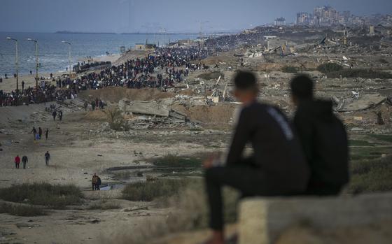 Two boys watch a crowd of Palestinians returning to northern Gaza, amid destroyed buildings, following Israel's decision to allow thousands of them to return for the first time since the early weeks of the 15-month war with Hamas, Monday, Jan. 27, 2025. (AP Photo/Abdel Kareem Hana)