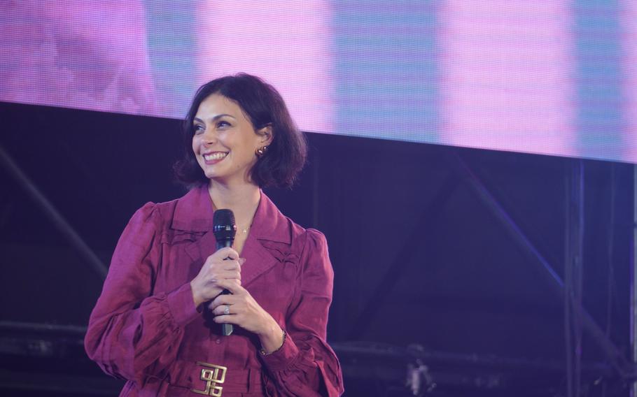 A woman in a magenta dress smiles as she holds a microphone.