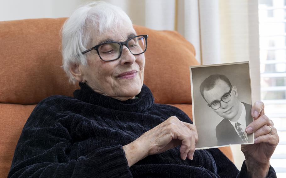 A woman with white hair and glasses holds a photo of her deceased husband.