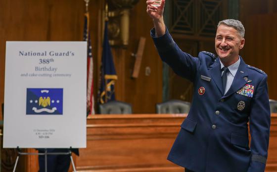 The head of the National Guard Bureau raises a glass while standing next to a poster announcing the National Guard’s 388th birthday.