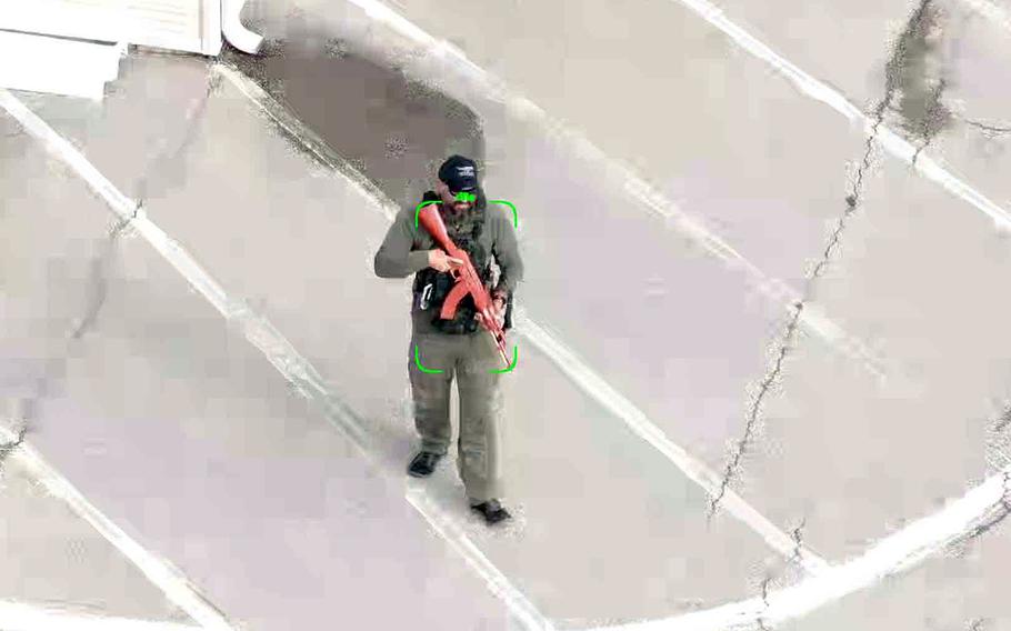 A man wearing tactical gear carries an automatic rifle as part of a test of AI software.