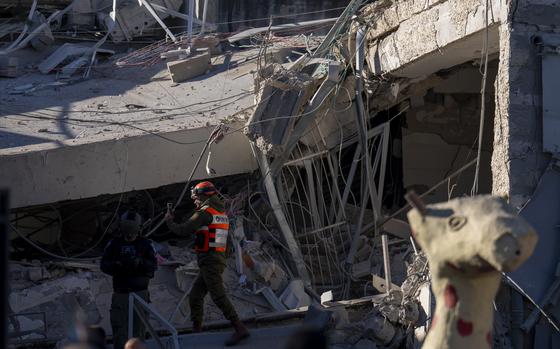 A man in a reflective vest walks toward a building frame that is partially collapsed and covered with debris in Ramat Gan.