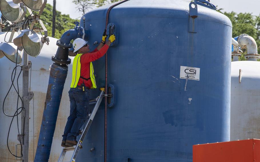 A man in a yellow reflective vest stands on a ladder propped up against a blue water tank.