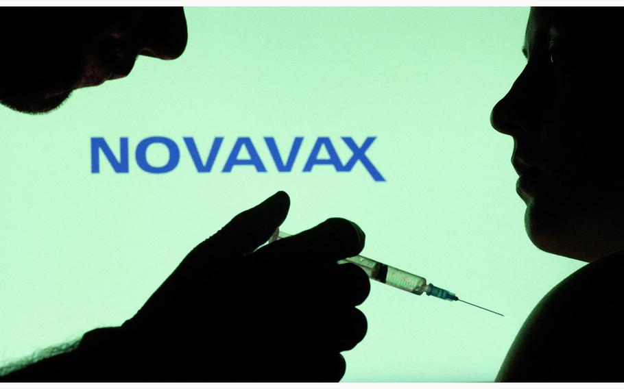 People pose with a needle-tipped syringe in front of a Novavax logo as seen in December 2021.
