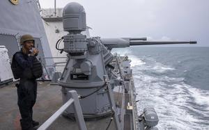 A U.S. seaman stands next to a 25mm machine gun on the deck of a destroyer.