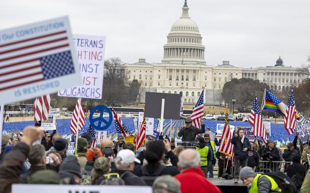 Group of protesters holding American flags and signs with the U.S. Capitol in the background.