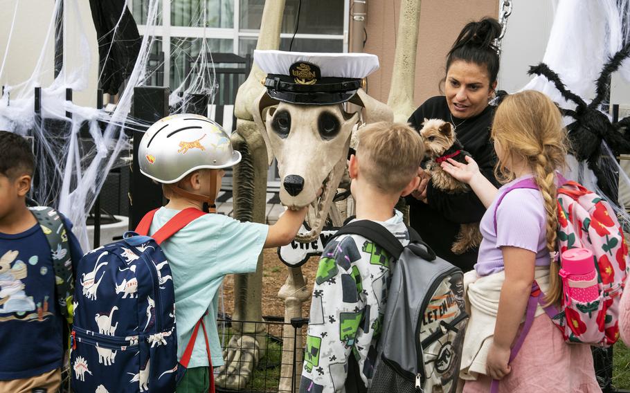 A group of children gather around a Halloween decoration of a skeletal dog.