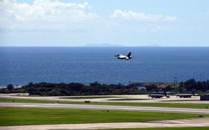 A plane flies over a runway with a beautiful blue ocean view in the background.