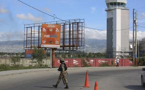 A uniformed officer holding a rifle walks across a street by an airport.