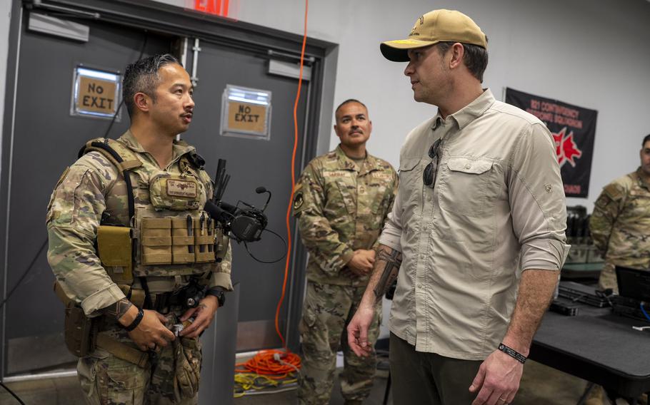 A service member, right, stands and talks with Hegseth as another service member watches them.