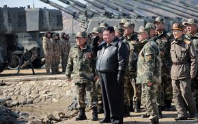 North Korean leader Kim Jong Un raises a hand to his head while surrounded by military members in uniform outside.