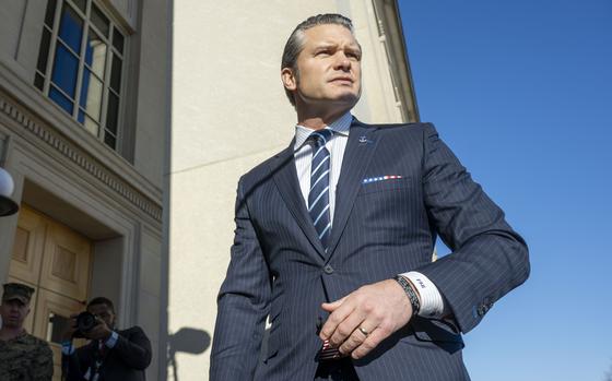 A man in a dark suit and tie, seen from below, stands outside a door to the Pentagon.