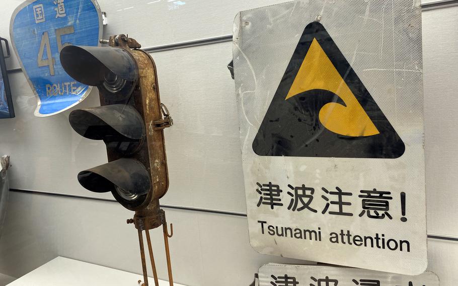 A damaged stoplight and weathered warning sign reading “Tsunami attention” sit in a museum exhibit.