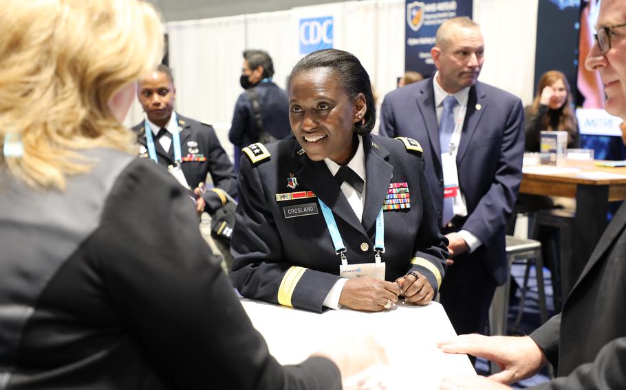 Crosland in uniform speaks with another woman at a conference surrounded by others. 