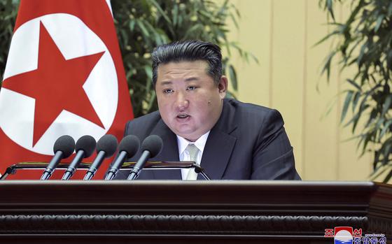 The North Korean leader speaks into a row of microphones with the North Korean flag in the background.