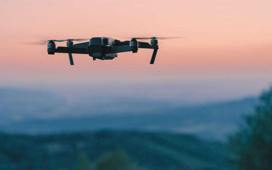 A drone in the air against and orange sky.