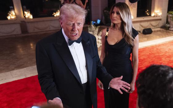 Donald Trump, wearing a tuxedo, speaks with reportes while standing on a red carpet next to wife Melania Trump.