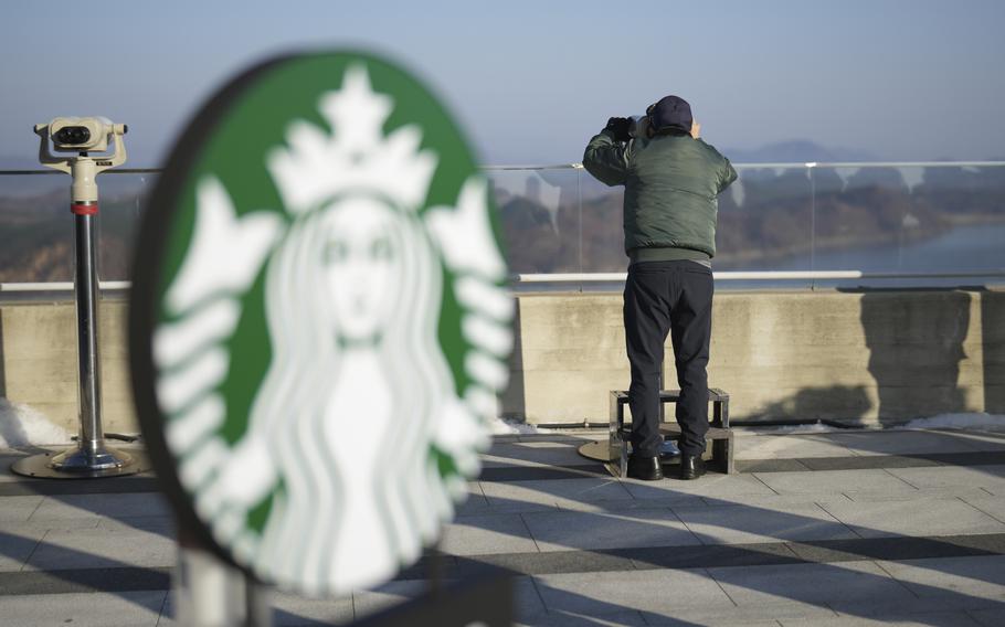 A Starbucks sign is visible in the foreground as a man looks through a tower viewer.