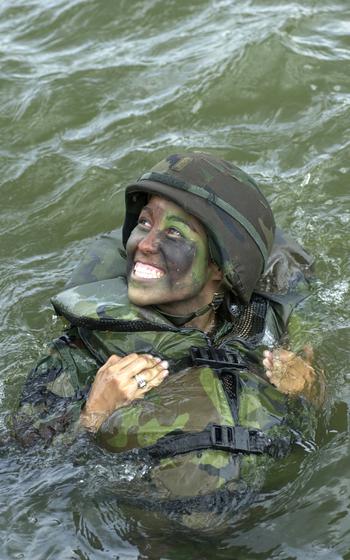 A female soldier looks up and smiles while floating in water.