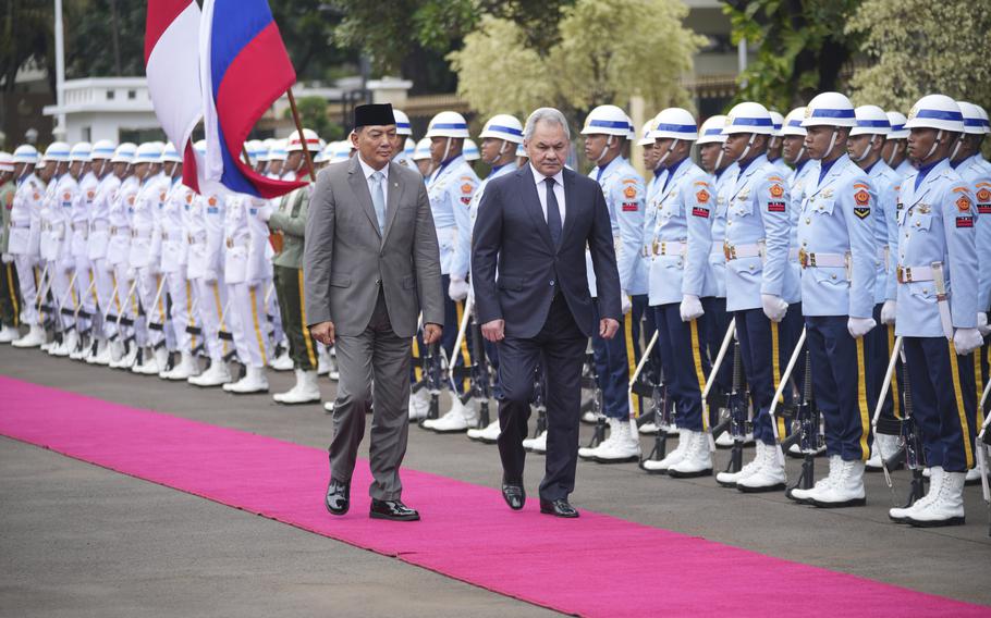 Two men walk down a pink carpet in front of rows of honor guards.