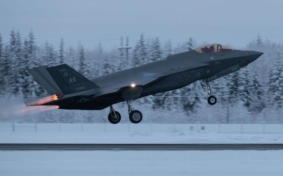 A military fighter jet takes off with a snowy treeline in the background.