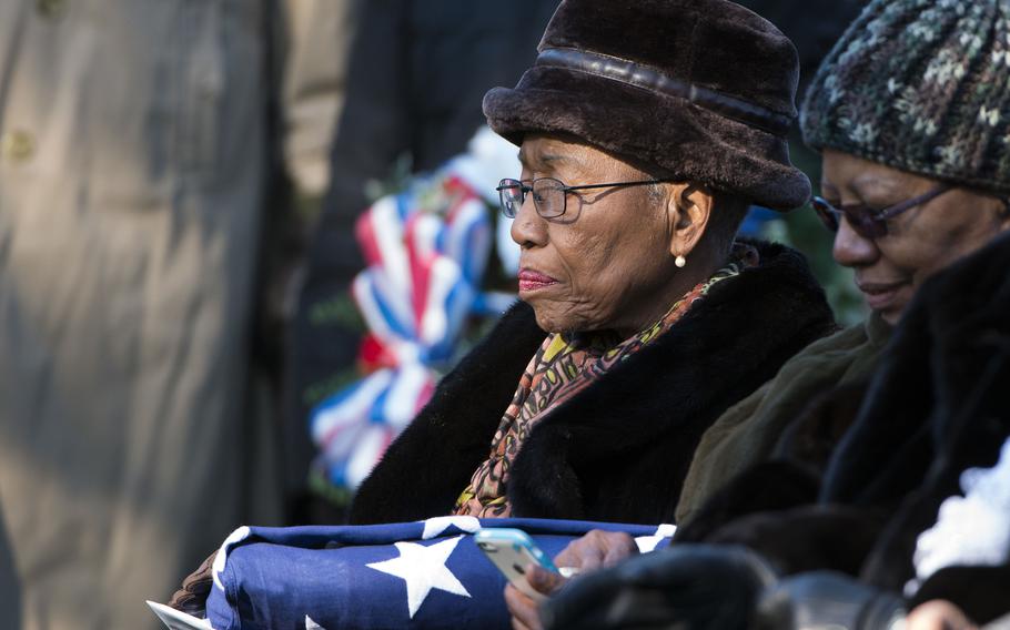 An elderly woman is seen in a black coat and fur hat.