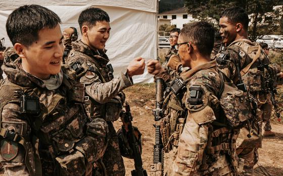 An American soldier fist-bumps with a South Korean soldier outside a large tent.