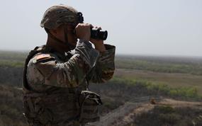 A soldier watches the border with binoculars.