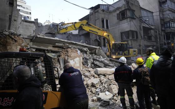 Resuce workers use an excavator to clear debris from a destroyed building.