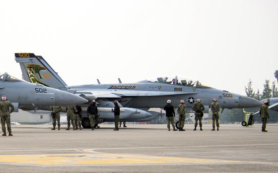 Pilots wearing helmets stand in front of a grounded plane.