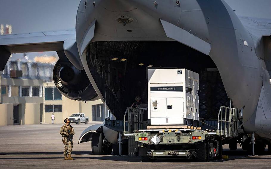 A U.S. service member, left, stands guard on Wednesday, May 15, 2024, as supplies are offloaded from a U.S. Air Force C-17 cargo plane on the tarmac at Toussaint Louverture International Airport in Port-au-Prince, Haiti. The plane was carrying supplies for the camp being built for Kenyan police officers who will lead a Multinational Security Support mission into Haiti. 