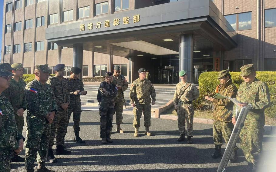 Philippines marines and Japan Ground Self-Defense Force members stand outside a large building.