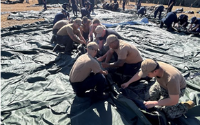 Several sailors on their knees building tents.