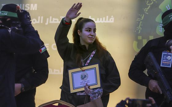 An Israeli woman with long, dark hair raises her hand and waves to a crowd as she is released from captivity.