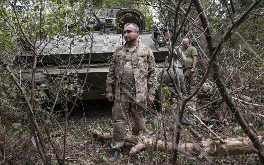 Ukraine soldiers stand in front of a military vehicle.