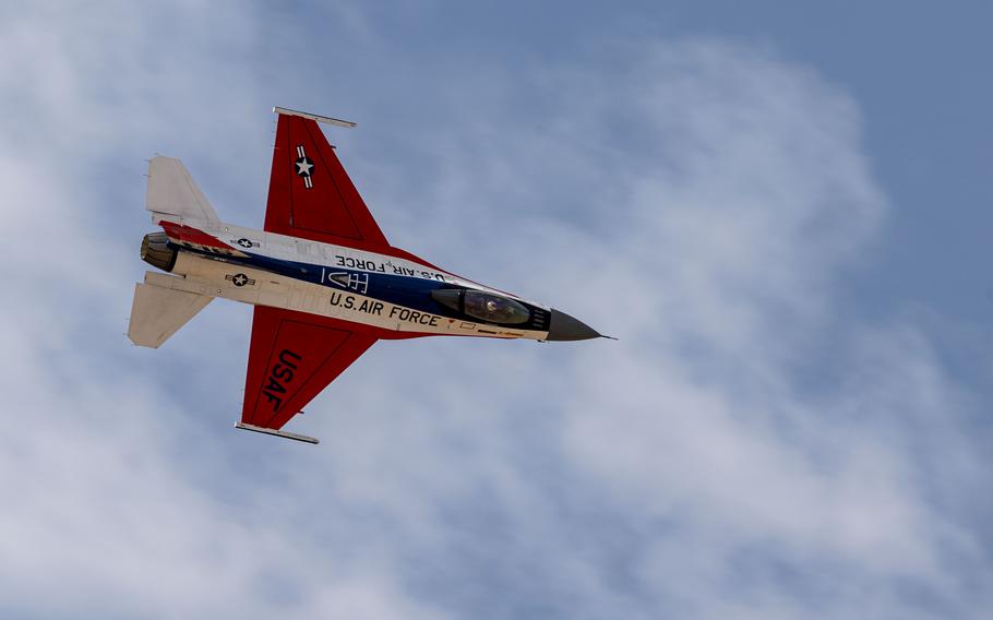 A view from below an F-16 in flight, blue sky and clouds above.