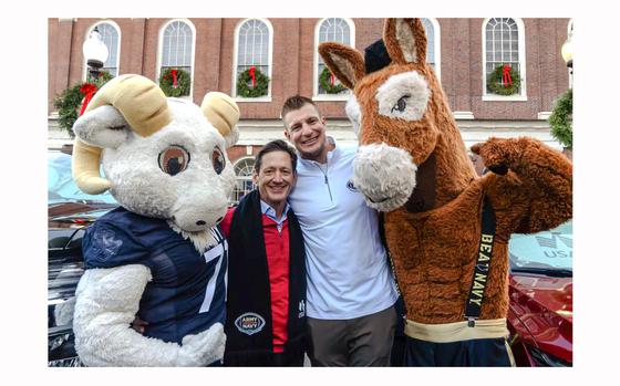 Former New England Patriots All-Pro tight end Rob Gronkowski hugs USAA CEO/President Wayne Peacock with BlackJack the Army Mule mascot and Bill the Navy Goat mascot on the sides.
