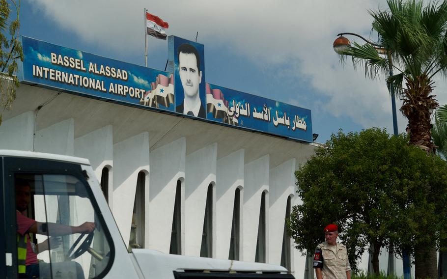 A car drives past a white building topped with a picture of the now-exiled Syrian president and a Syrian flag.