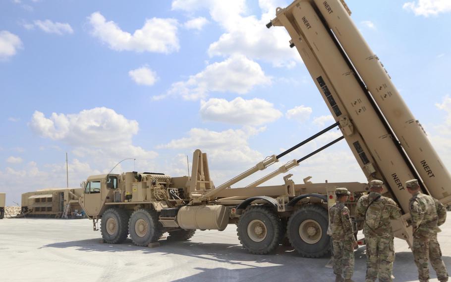 Soldiers stand in front of a missile defense system.