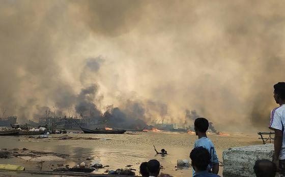 This handout photo provided by the Arakan Army shows people looking at flames rising after an airstrike by the ruling military in Kyauk Ni Maw village, in Ramree township, also pronounced Yanbye, in Rakhine state, Myanmar, Wednesday, Jan.8, 2025. (The Arakan Army via AP)