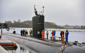 Workers stand atop a submarine where an American flag is afixed.