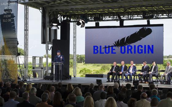 An Air Force leader stands at a podium on a stage above a crowd, with other men in suits seated away from him on the stage.