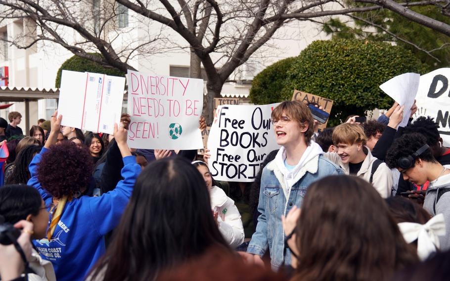 High school students hold signs reading, “Diversity needs to be seen” and “Free our books, free our stories” while a student speaks.