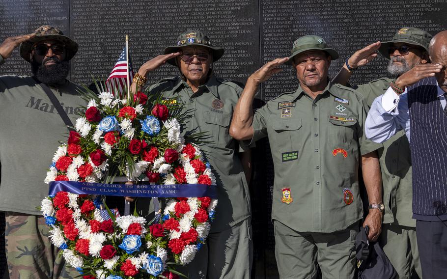 Men in their vintage uniforms salute in front of the Vietnam Veterans Memorial.