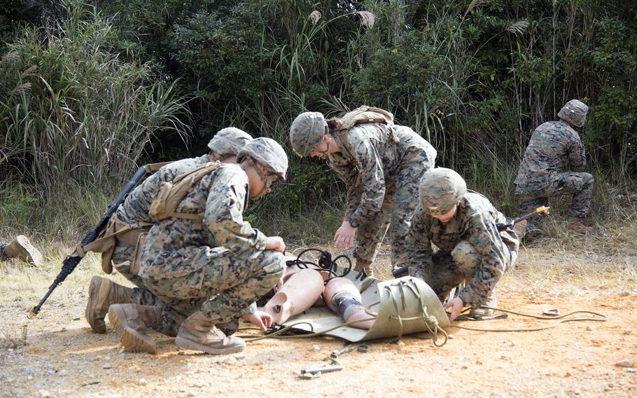 A group of Marines surround a stretcher with a dummy on it.